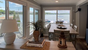 Uma área de refeições com vista para um lago, uma mesa com cadeiras, um abajur, uma planta em vaso e um candeeiro rústico.