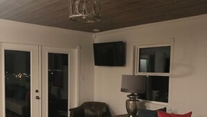 A living room with a white sofa, a leather chair, a wooden ceiling, and a TV mounted on the wall. - HOTLIPS AT COLLINWOOD upstairs Price is on the website  Down stairs $125 extra (Hiawassee)