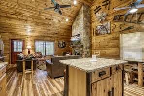 Cozy cabin-style interior with a stone fireplace, wooden ceiling, and central island.