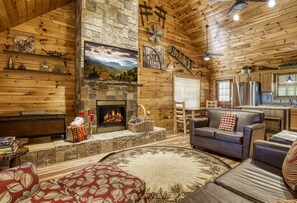 A cozy cabin interior with a stone fireplace, wooden walls, a sofa, and a dining area. - Close to Pigeon Forge, Private Putt Putt, Movie theatre, Mountain View and More (Sevierville)