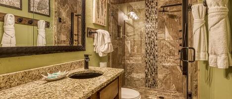 Une salle de bain dotée d’un comptoir en granit, d’une douche à parois de verre et de toilettes.