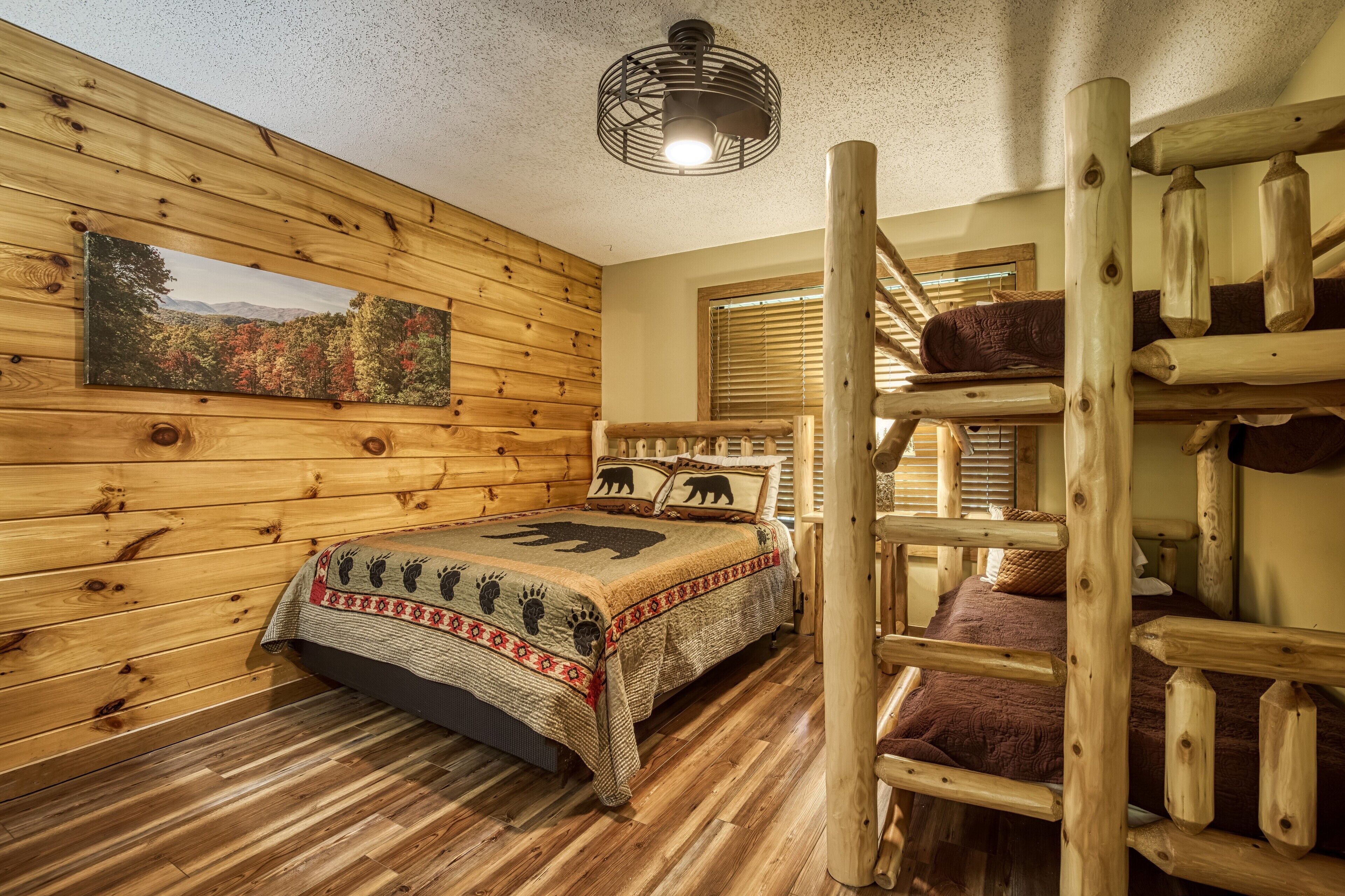 A log cabin bedroom with a bunk bed, a wooden ceiling, a painting of a forest, and a window with blinds.