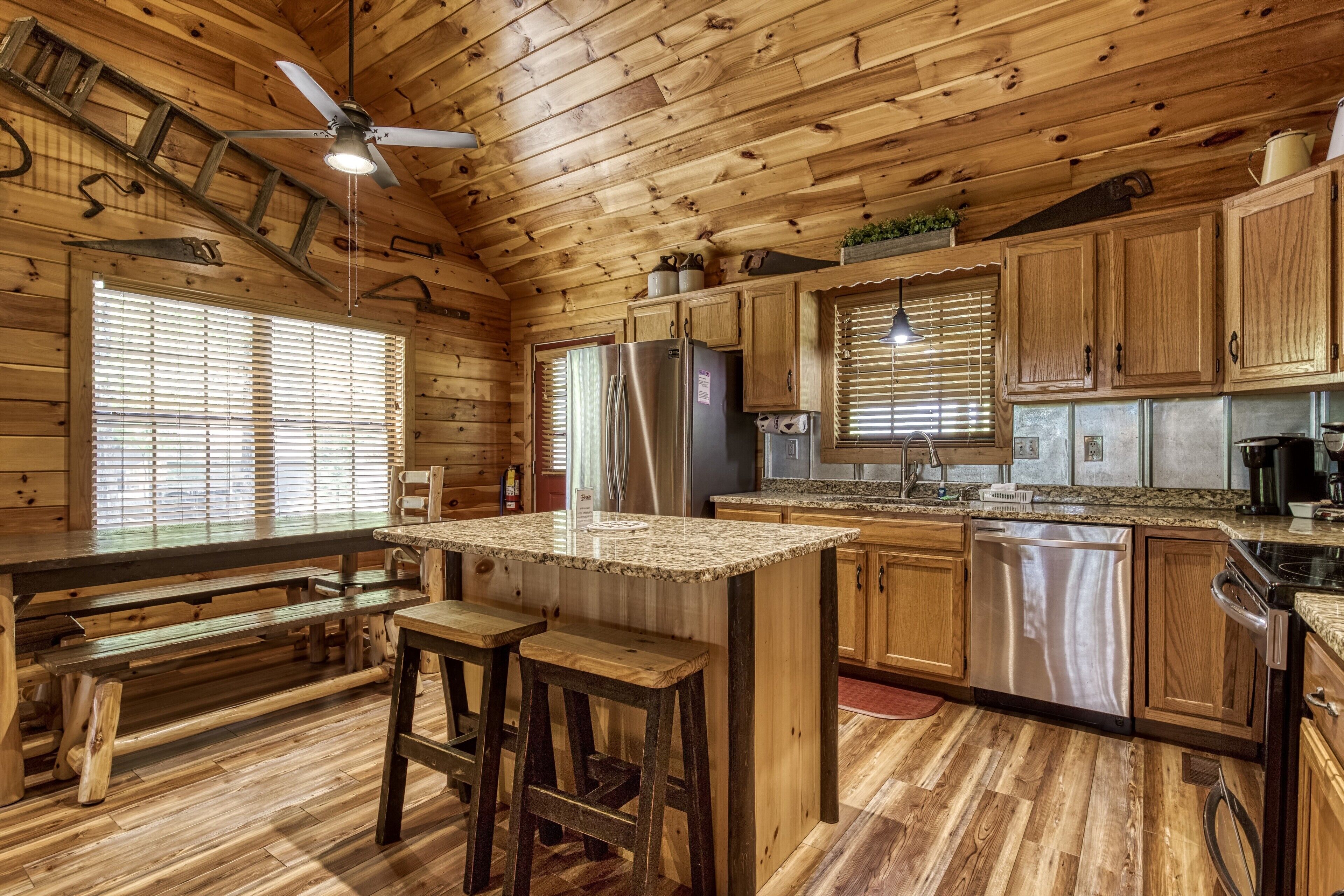 A wooden cabin kitchen with a central island, wooden benches, and a ceiling fan.