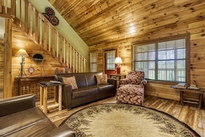 Cozy cabin interior with a wooden staircase, leather sofa, and floral-patterned armchair.