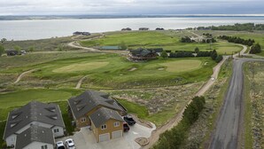 Una casa grande con garaje, entrada para vehículos y un campo de golf al fondo.