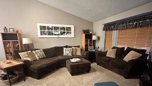 A living room with a sectional sofa, a small ottoman, a wooden coffee table, and a bookshelf. - Welcome To Our "Home To The Outdoors" (La Pine)