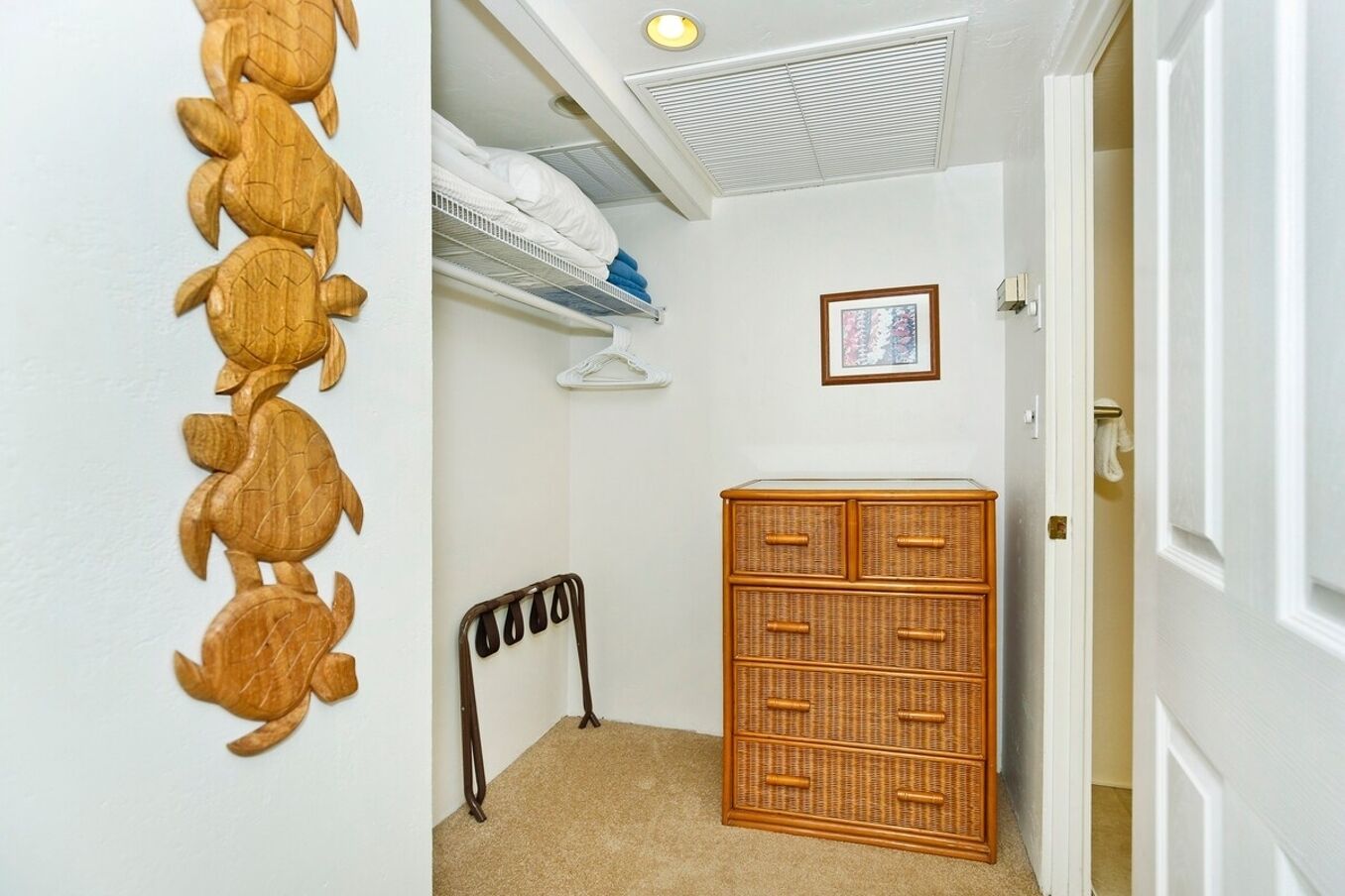 Een gang met een houten wanddecoratie, een rieten dressoir en een bed met witte lakens.