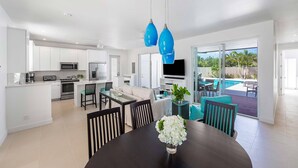 A modern kitchen with white cabinets, a dining area with a dark table and chairs, and a large window overlooking a pool.