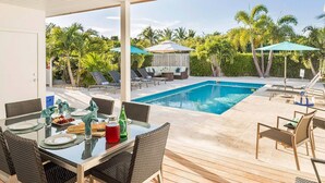 A poolside dining area with a table set for two, surrounded by lounge chairs and umbrellas, overlooking a swimming pool.