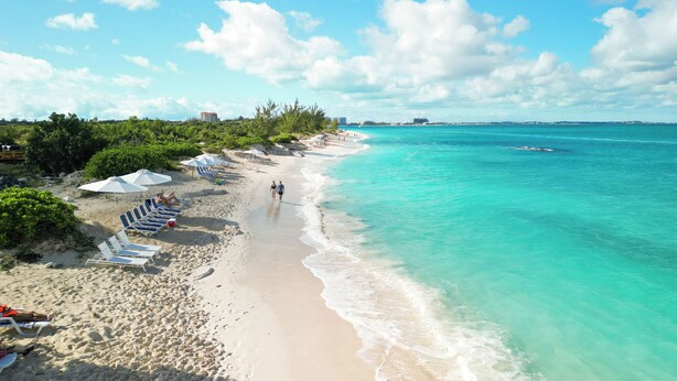 A beach with clear turquoise water, a sandy shore, and umbrellas providing shade.
