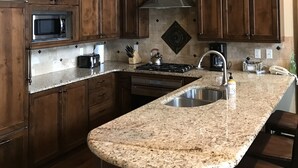 Una cocina con armarios de madera oscura, encimera de granito, pileta de acero inoxidable y lámparas colgantes.