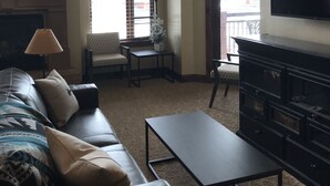 Amplia sala de estar con un sofá grande, una mesa de centro y un televisor montado en la pared. Varias ventanas ofrecen luz natural y vistas al exterior.