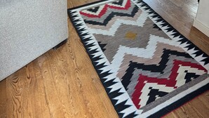 Een woonkamer met een grijze bank, een houten eettafel met stoelen, en twee gestreepte tapijten op de houten vloer.