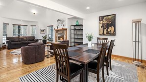 A spacious living room with a fireplace, a dining area with a wooden table and chairs, and a large bull painting on the wall. - Blue Star Creekside Lodge  (Columbia Falls)