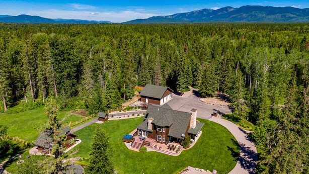 A large house surrounded by a dense forest with a mountain range in the background. - Blue Star Creekside Lodge  (Columbia Falls)