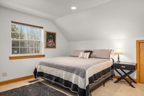 A bedroom with a bed, a nightstand, a lamp, a window, and a painting on the wall.