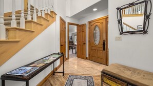 A hallway with a wooden staircase, a bench, a door with a glass panel, and a wall-mounted mirror. - Blue Star Creekside Lodge  (Columbia Falls)