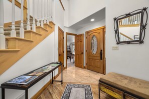 A hallway with a wooden staircase, a bench, a door with a glass panel, and a wall-mounted mirror. - Blue Star Creekside Lodge  (Columbia Falls)