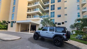 Ein modernes Hotel mit mehrstöckiger Bauweise, einer überdachten Eingangszone und einem Parkplatz mit einem weißen SUV.