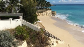 Ein Strand mit einem weißen Gebäude, Palmen und wolkenlosem, blauem Himmel.