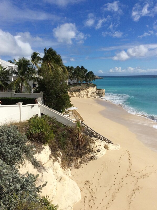 A beach with a white building, palm trees, and a clear blue sky.