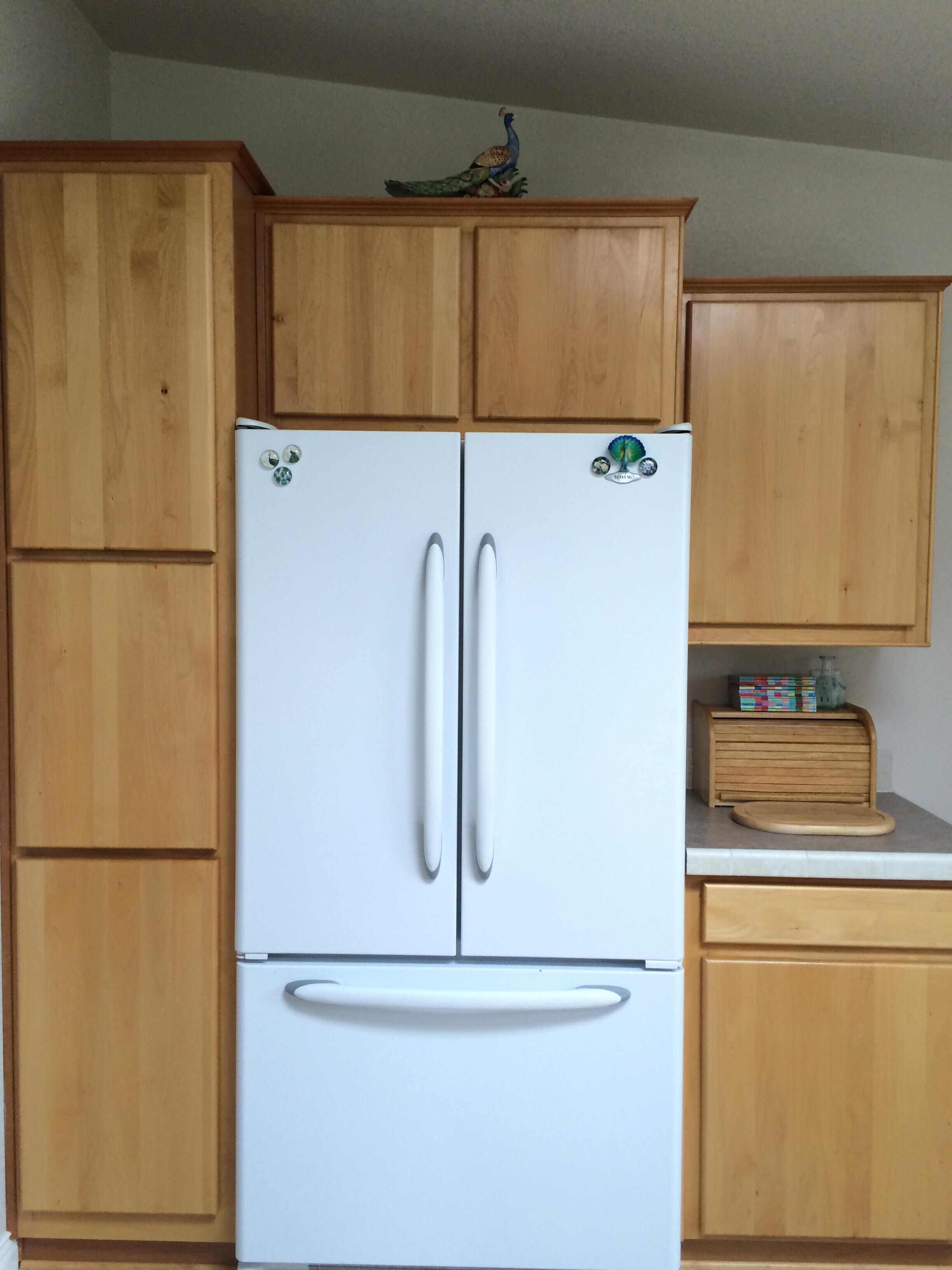 Een witte koelkast met twee deuren en een vriesvak, in een keuken met houten kasten en een aanrecht.
