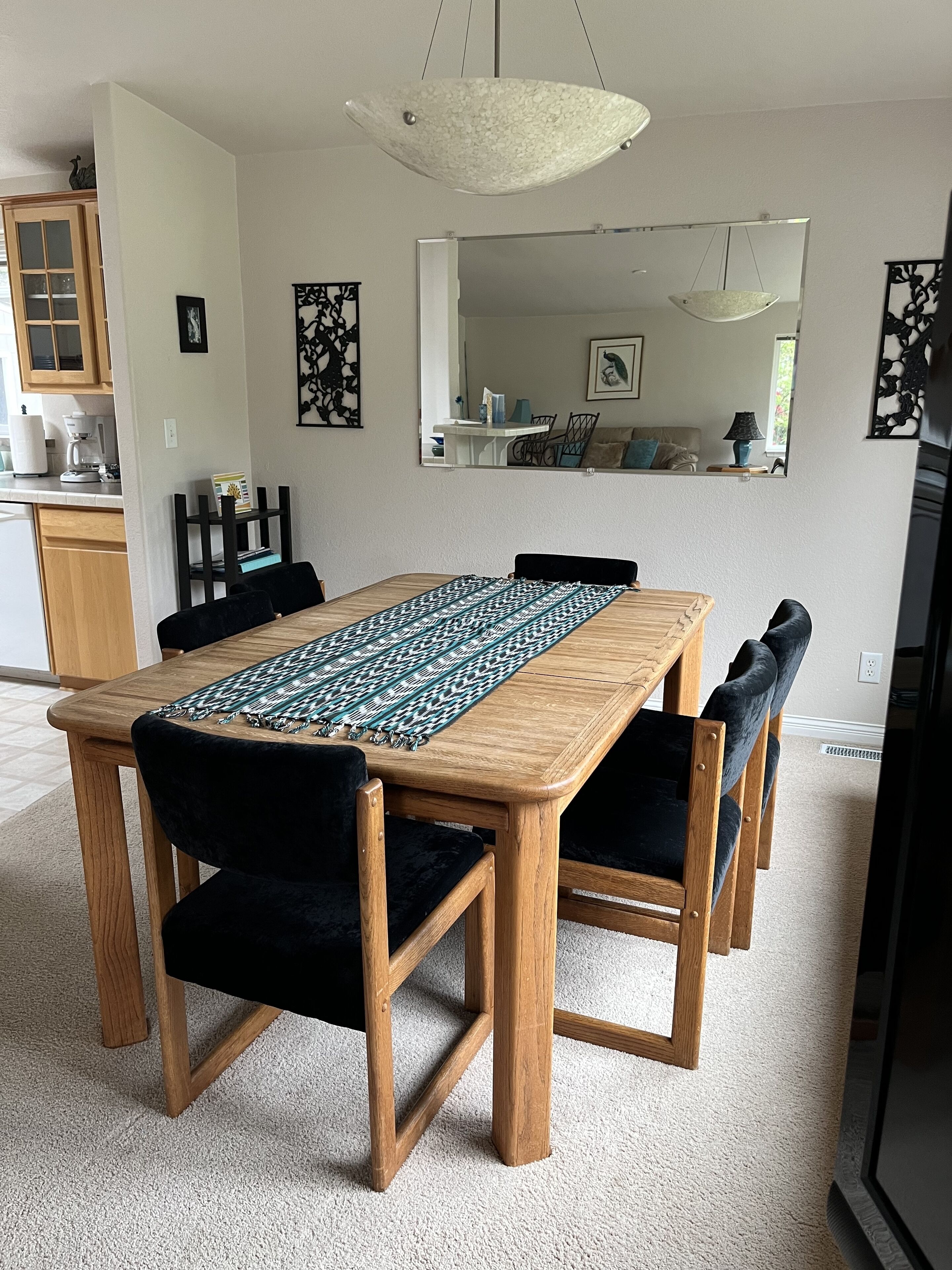 A dining area with a wooden table, black upholstered chairs, a patterned runner, and a hanging light fixture.