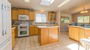 A modern kitchen with wooden cabinets, a central island, a microwave, an oven, and a sink. There are skylights and a chandelier. - Private Beach Access, Clean, Comfortable Home between Sequim & Port Angeles  (Port Angeles)