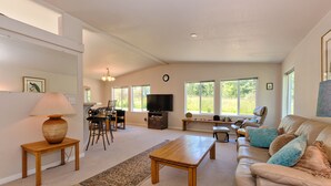 A spacious living room with a large sofa, a coffee table, a TV, and a dining area with chairs and a table. - Private Beach Access, Clean, Comfortable Home between Sequim & Port Angeles  (Port Angeles)