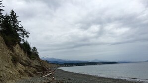 A rocky beach with a cliff on one side and mountains in the distance. - Private Beach Access, Clean, Comfortable Home between Sequim & Port Angeles  (Port Angeles)