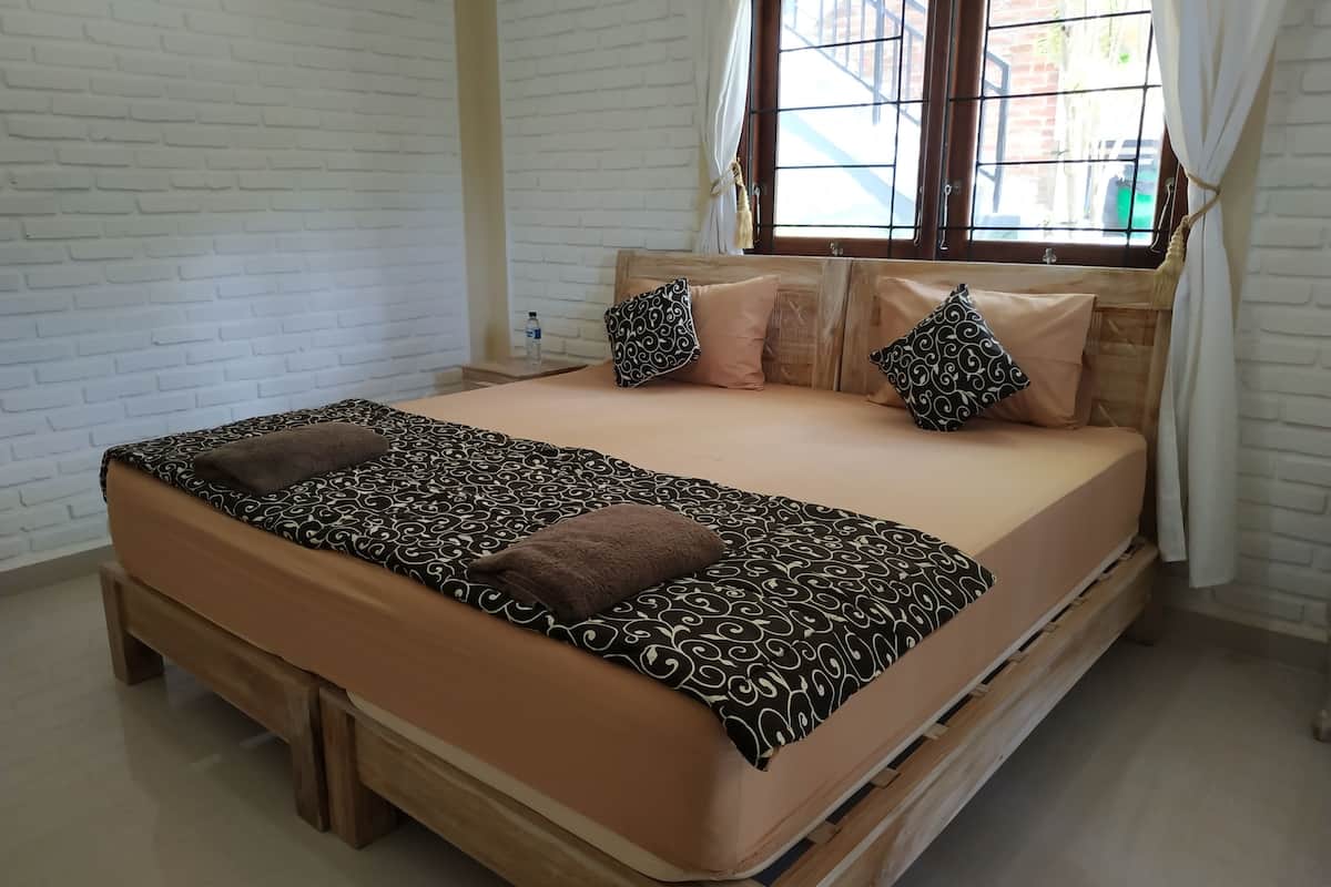 A bed with a patterned bedspread and pillows, a wooden headboard, and a window with curtains.