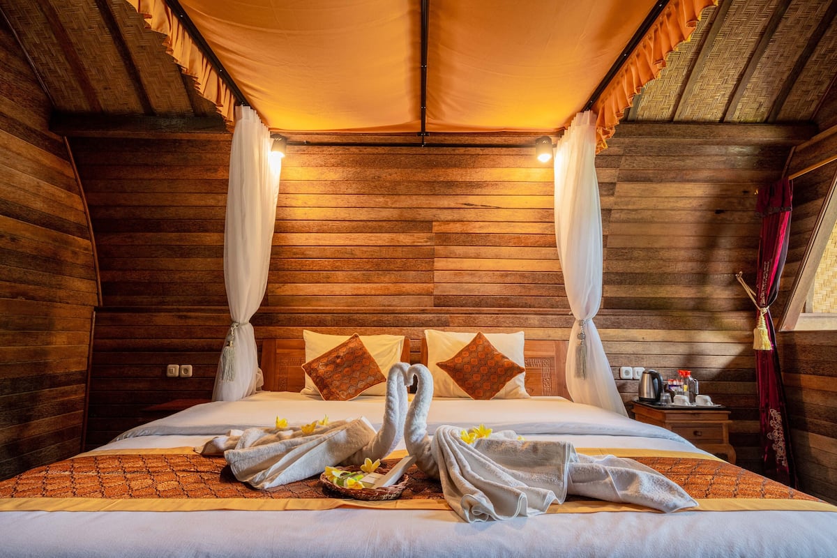 A wooden room with a bed, curtains, and a tray with towels.