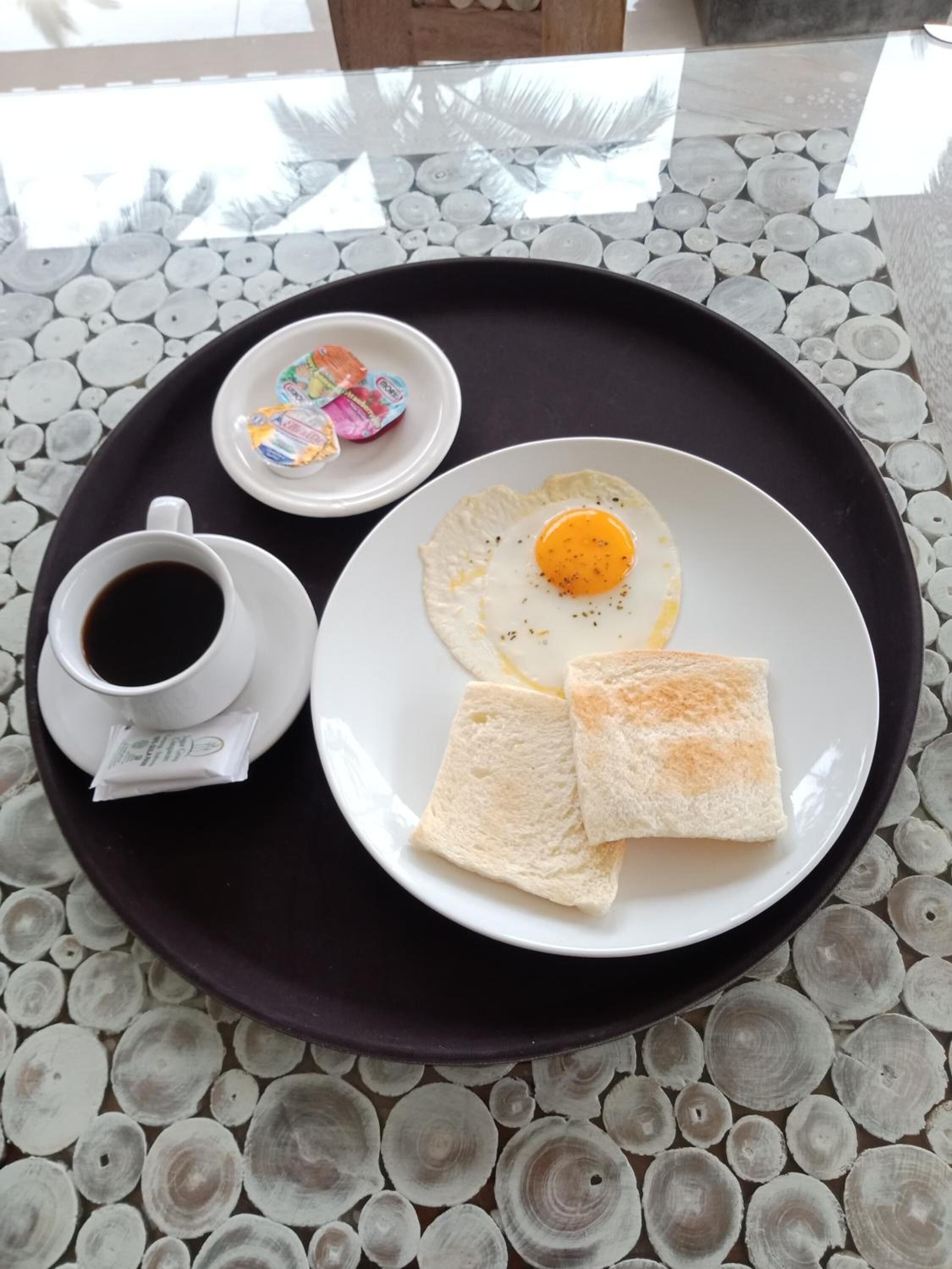 A breakfast tray with a fried egg, toast, a cup of coffee, and a small dish of butter on a table with a unique tile pattern.