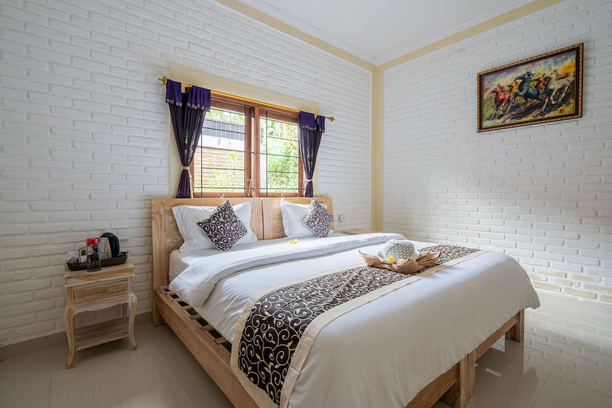 A neatly made bed with a wooden frame, a nightstand with a lamp, and a window with purple curtains.