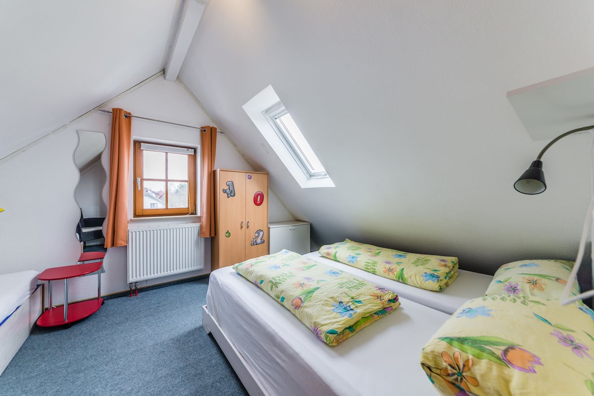A small, triangular room with a bed, a desk, and a window.