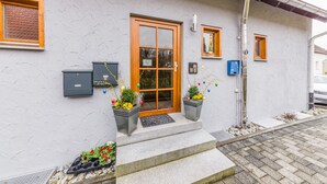 Un bâtiment avec une porte en bois, un petit porche orné de plantes en pot et une boîte aux lettres.