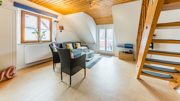 Un vaste espace de vie doté d’un haut plafond, d’un ensemble de canapés, d’une table à manger et d’un escalier.