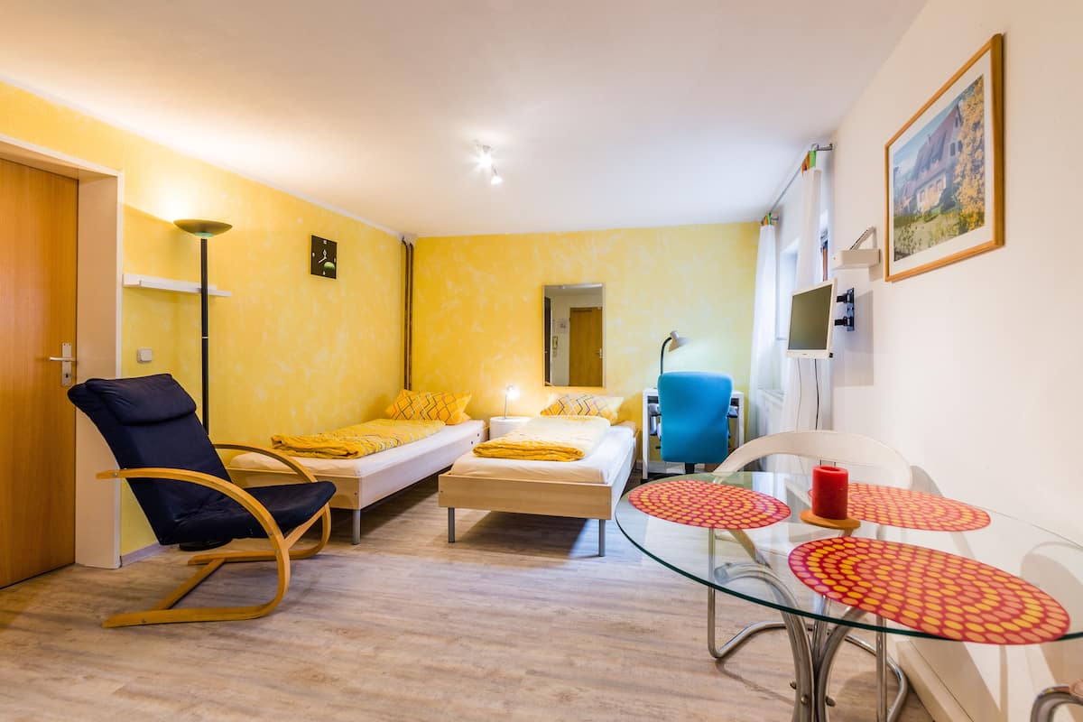 A compact room with a bed, a sofa, a rocking chair, and a small glass table with red coasters.