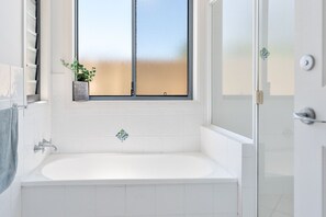A modern bathroom with a large window, a bathtub, and a shower area.