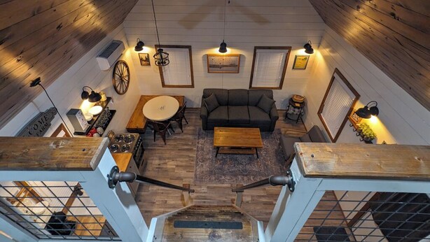 A high-ceilinged room with a ceiling fan, wooden walls, a dining area with a table and chairs, a sofa, and a staircase leading to an upper level. - Black Hills Farmhouse (Custer)