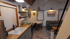 A rustic kitchen with wooden countertops, a sink, a stove, and a dining area with a table and chairs. There is a sofa and a clock on the wall. - Black Hills Farmhouse (Custer)