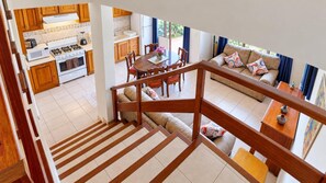 A modern kitchen with wooden cabinets, a dining area with a round table and chairs, and a living room with a sofa and cushions. - Rio Copey 2 townhouse near the beach in Jaco (Jaco)