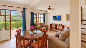 Bright living and dining area with garden-facing glass doors at Rio Copey 2 in Jacó.