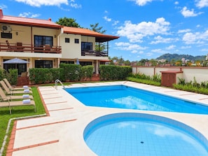 A hotel with a swimming pool, lounge chairs, and a view of the surrounding landscape.