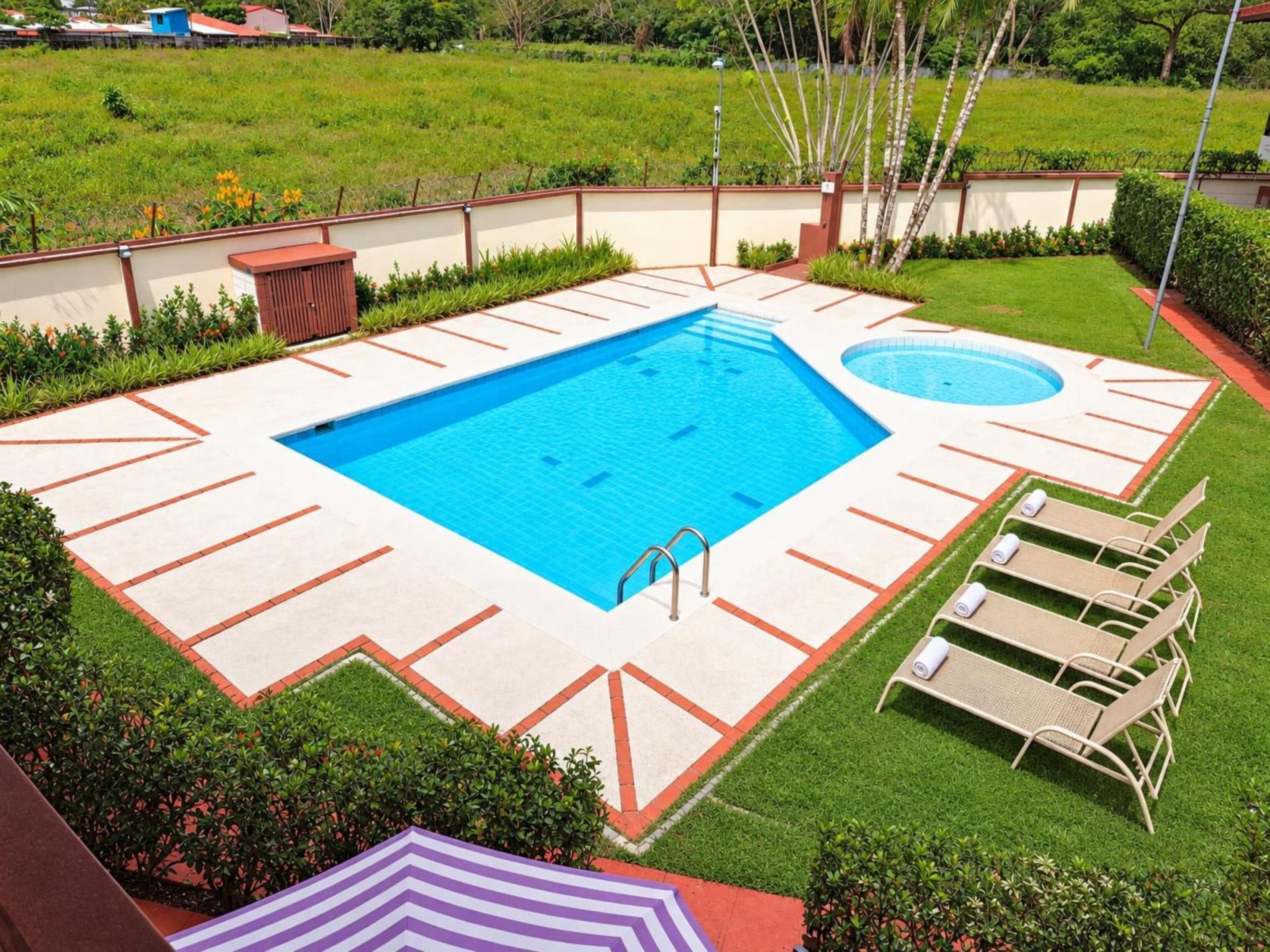 Une piscine rectangulaire dotée d’un plongeoir et d’une plus petite piscine circulaire, le tout entouré d’une pelouse et d’un petit muret.