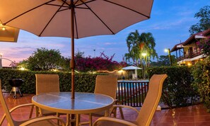 An outdoor patio with a round table and chairs, a large umbrella, and a pool in the background. - Rio Copey 2 townhouse near the beach in Jaco (Jaco)