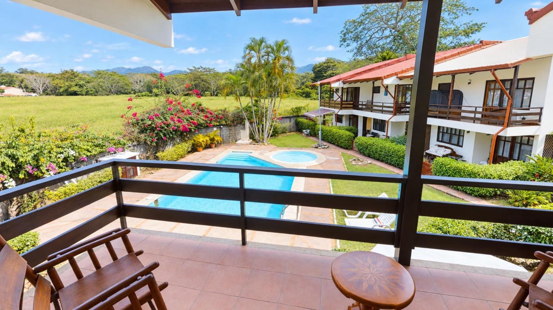 Un balcon donnant sur une piscine, un immeuble de deux étages et un jardin luxuriant.