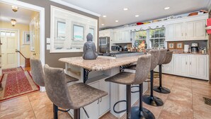A kitchen with a granite countertop, white cabinets, and a red rug.
