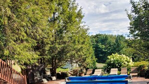 A rectangular swimming pool with a wooden deck surrounding it, equipped with lounge chairs and a small table.