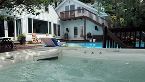Un bain à remous avec vue sur une piscine et une maison dotée d’un balcon.